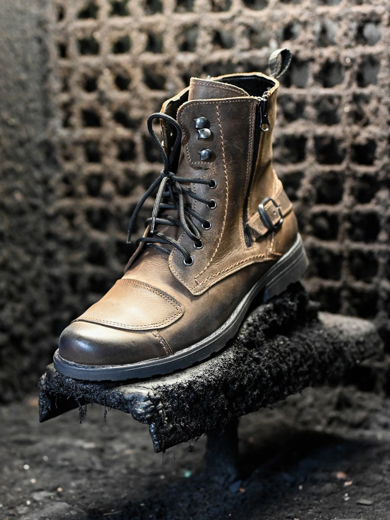May include: A brown leather ankle boot with black laces and a zipper on the side. The boot has a buckle on the side and a thick black sole.