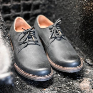 May include: A pair of black leather lace-up shoes with a slightly distressed finish. The shoes have a rounded toe and a thick sole.