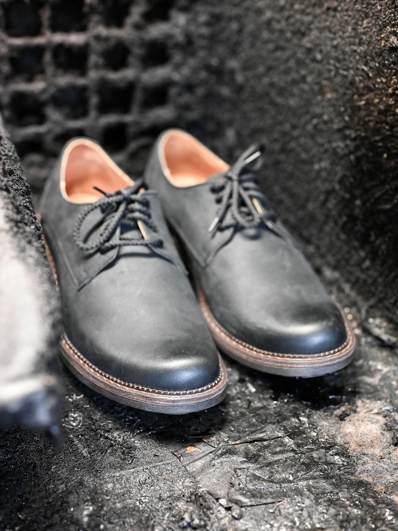 May include: A pair of black leather lace-up shoes with a slightly distressed finish. The shoes have a rounded toe and a thick sole.