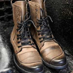 May include: A pair of brown leather boots with black laces. The boots have a round toe and a thick sole.