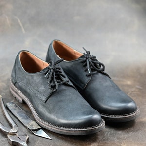 May include: Two black leather lace-up shoes with a brown leather background.
