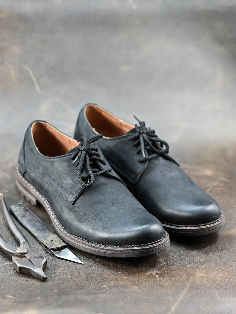 May include: Two black leather lace-up shoes with a brown leather background.