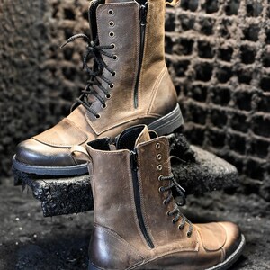 May include: Two brown leather boots with black laces and zippers. The boots have a rugged look and are made of distressed leather.