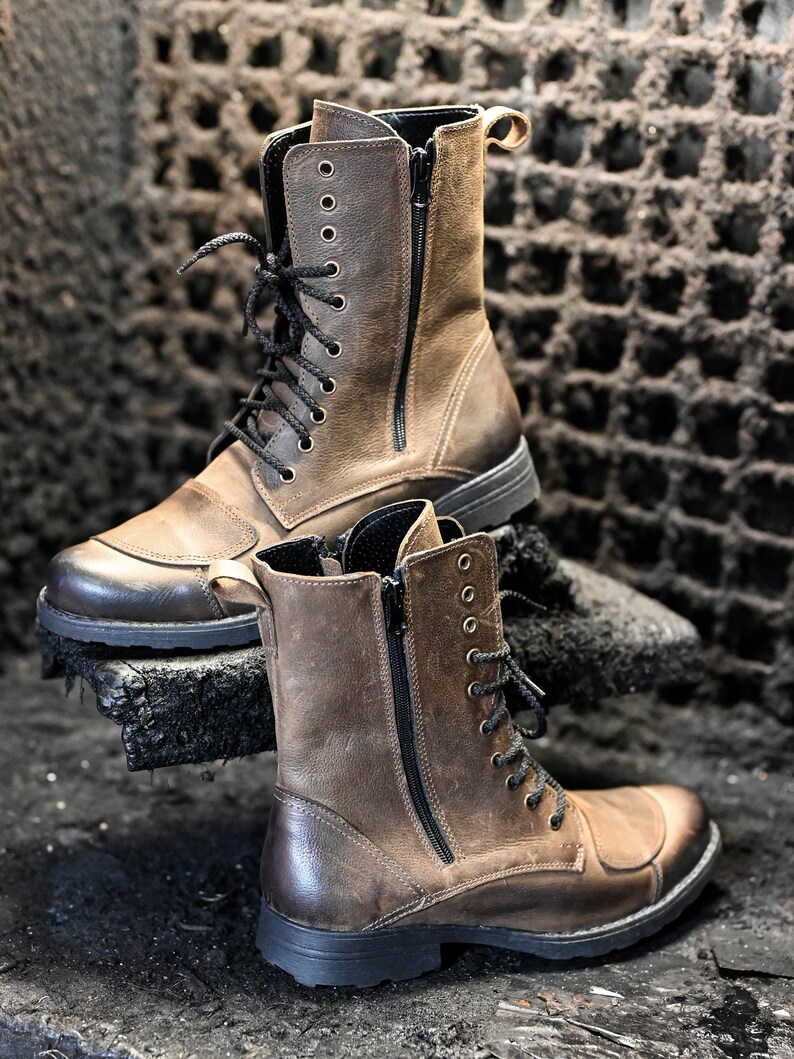 May include: Two brown leather boots with black laces and zippers. The boots have a rugged look and are made of distressed leather.