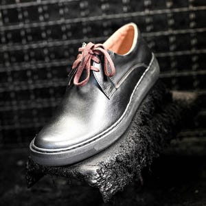 May include: Black leather lace-up shoe with a brown shoelace. The shoe is sitting on a black surface.