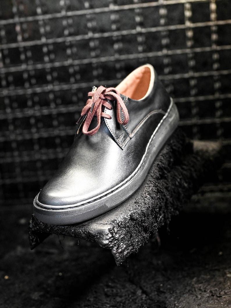 May include: Black leather lace-up shoe with a brown shoelace. The shoe is sitting on a black surface.