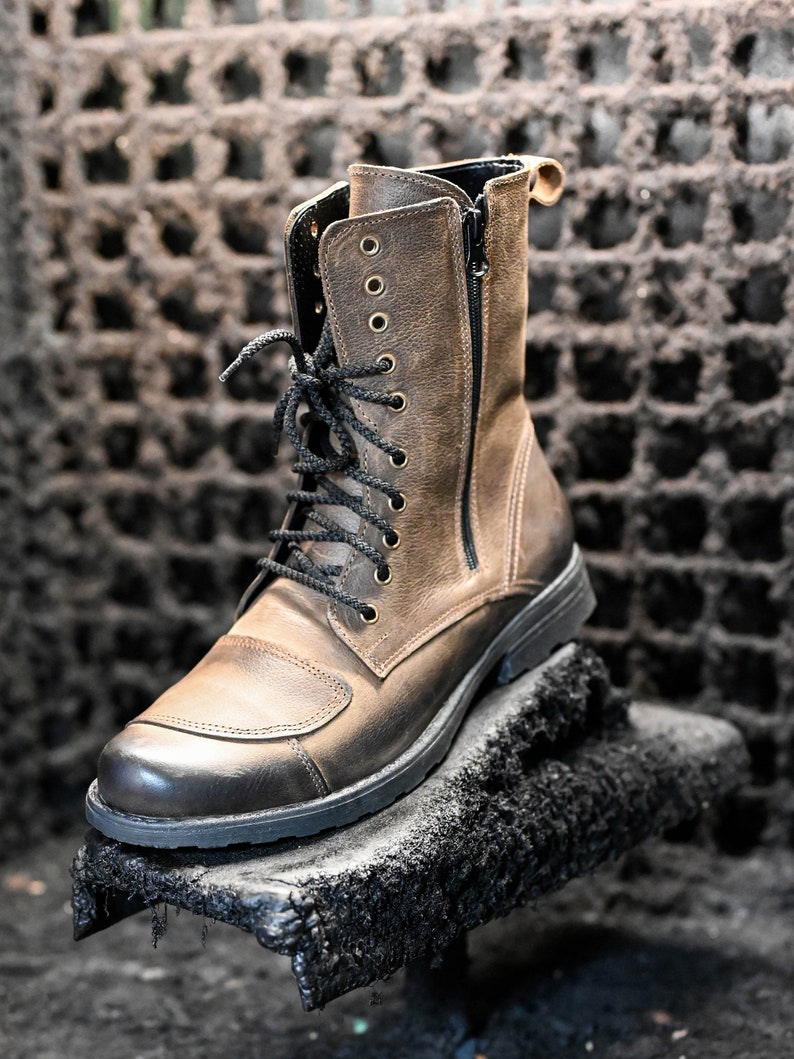 May include: A brown leather ankle boot with black laces and a zipper on the side. The boot has a thick black sole and is sitting on a black surface.