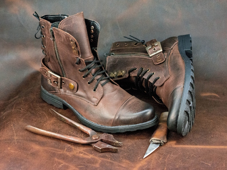 May include: Two brown leather boots with buckles and laces, a pair of pliers, and a small knife on a brown leather surface.