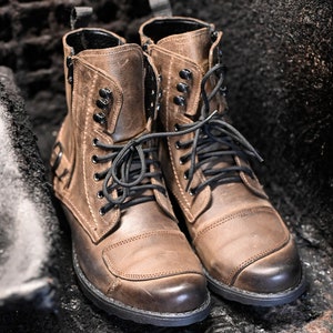 May include: A pair of brown leather boots with black laces and buckles. The boots have a rugged look and are made of high-quality leather.