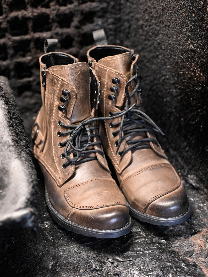 May include: A pair of brown leather boots with black laces and buckles. The boots have a rugged look and are made of high-quality leather.