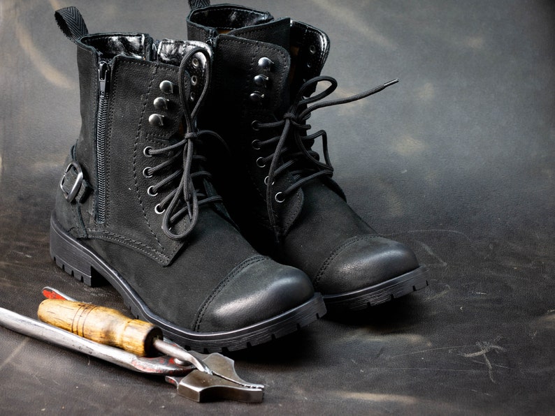 K&ouml;nnte beinhalten: Ein Paar schwarze Lederstiefel mit Schn&uuml;rsenkeln und Schnallen. Die Stiefel haben einen robusten Look und sind aus hochwertigen Materialien gefertigt.