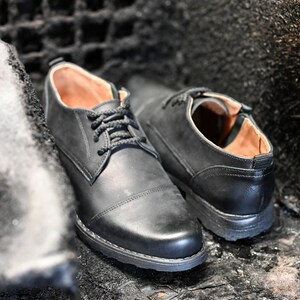 May include: Two black leather lace-up shoes with brown leather lining. The shoes are sitting on a dark, textured surface.
