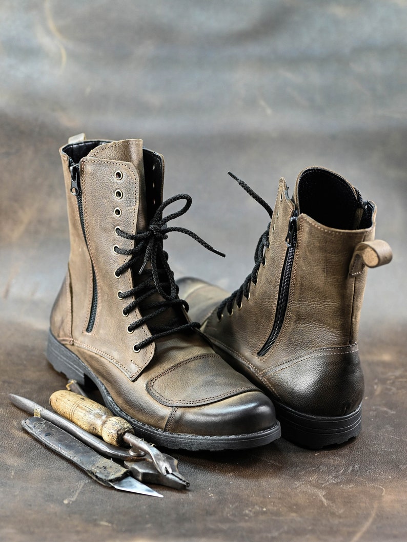 May include: A pair of brown leather boots with black laces and zippers. The boots have a rugged look and are made of distressed leather.