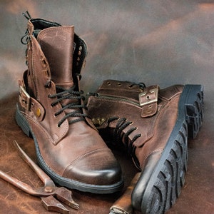 May include: Two brown leather boots with laces and buckles, a pair of pliers, and a small knife on a brown leather background.