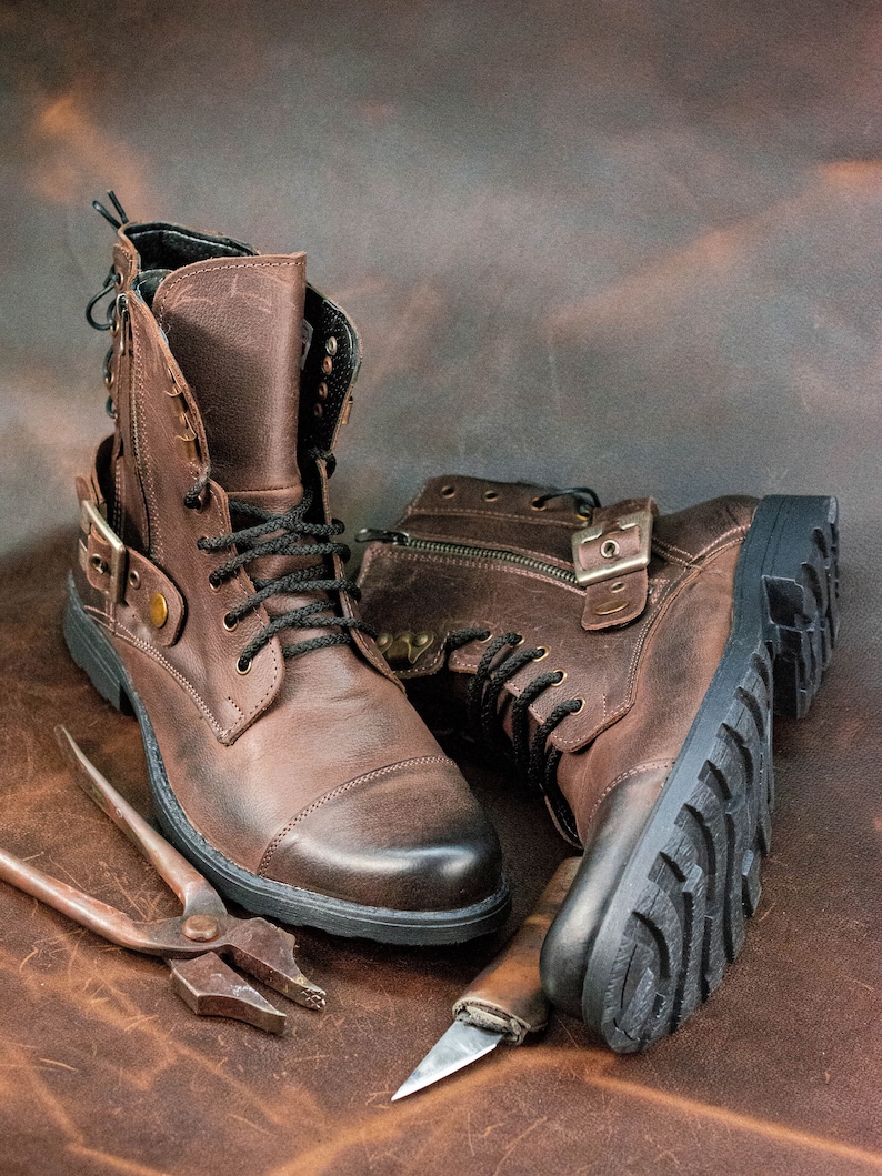 May include: Two brown leather boots with laces and buckles, a pair of pliers, and a small knife on a brown leather background.