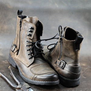 May include: A pair of brown leather boots with black laces and buckles. The boots have a zipper on the side and are made of distressed leather.