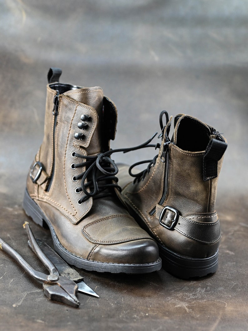 May include: A pair of brown leather boots with black laces and buckles. The boots have a zipper on the side and are made of distressed leather.
