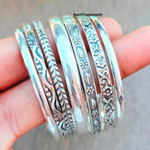 Puede incluir: Un conjunto de pulseras de plata con diseños intrincados, incluyendo patrones florales y de hojas. Las pulseras se muestran en una mano, mostrando su acabado pulido y su detallada artesanía. Adecuado para uso diario o ocasiones especiales.