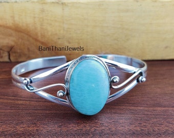 May include: A silver bangle bracelet with a light blue oval gemstone. The bracelet has a delicate, ornate design.