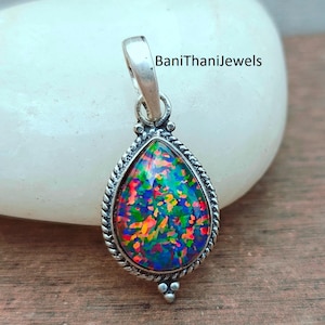 May include: A teardrop-shaped pendant with a vibrant, multicolored opal stone set in a silver-toned metal frame. The opal displays shades of blue, green, orange, and red. The frame has a rope-like border and small decorative accents. The text "BaniThaniJewels" is visible.