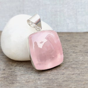 May include: A silver pendant featuring a large, rectangular, light pink rose quartz gemstone.