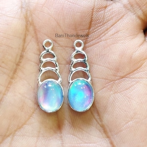 May include: A pair of silver earrings featuring iridescent blue and purple oval-shaped stones. The earrings have a delicate, layered design with a series of small circles.