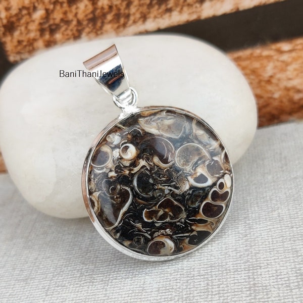 May include: A round silver pendant featuring a brown and white agate stone. The stone displays a swirling pattern of brown and white.