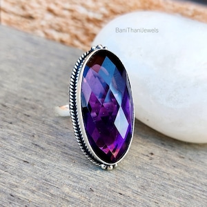 Könnte beinhalten: Ein silberner Ring mit einem großen, facettierten, ovalen Amethyst-Edelstein. Der Ring hat einen dekorativen, perlenbesetzten Rand um den Stein.