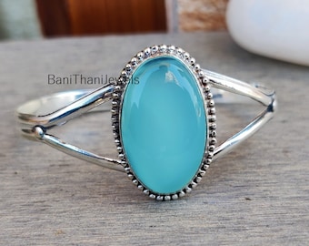 May include: A silver bangle bracelet with a light blue oval gemstone set in a beaded bezel. The bracelet has a delicate, openwork design.