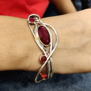 Peut inclure: Bracelet en argent avec trois accents de pierres précieuses rouges. Le bracelet a un design délicat et complexe.