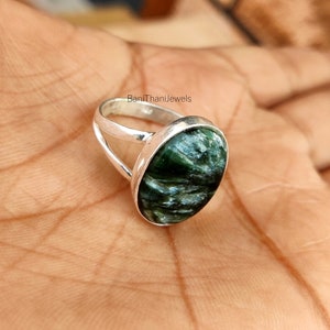 May include: A silver ring with a green and gray gemstone. The ring has a simple band with a split design.