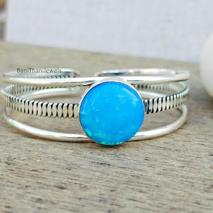 Peut inclure: Un bracelet jonc en argent avec une pierre d'opale bleue. Le bracelet a un design texturé et est composé de trois bandes.