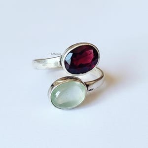 Peut inclure: Une bague en argent avec deux pierres ovales. La pierre supérieure est d'un rouge profond, et la pierre inférieure est vert pâle. La bague a un design enveloppant unique.