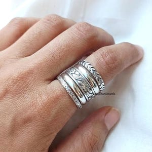 May include: A silver ring with multiple bands of varying widths and designs. The ring features floral, braided, and patterned details. The ring is worn on a finger against a white background. The text "BaniThaniJewels" is visible on the ring.