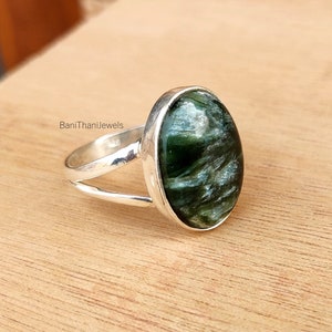 May include: A silver ring with a green and white oval gemstone. The ring has a split band design. BaniThaniJewels is printed on the band.