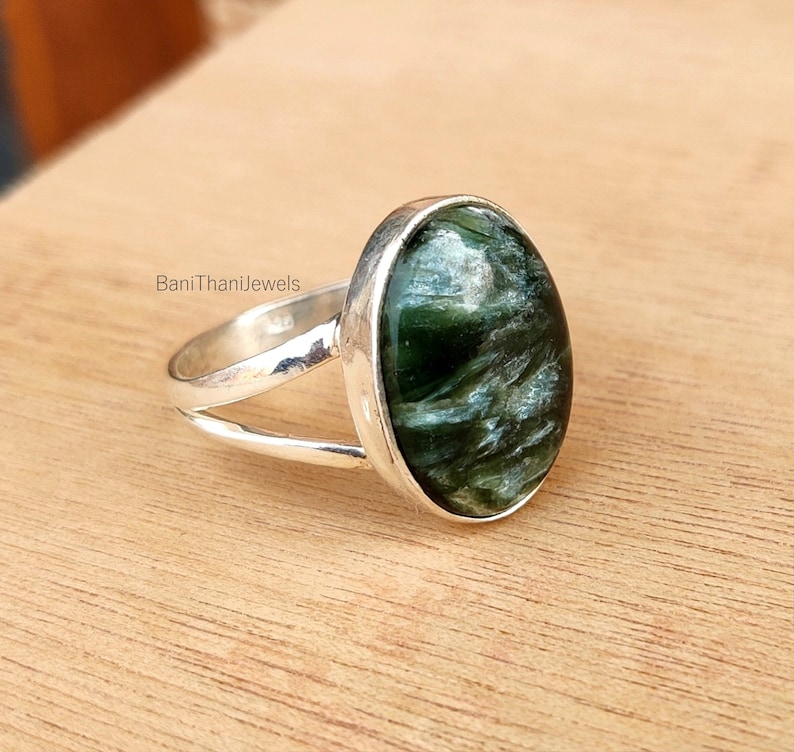 May include: A silver ring with a green and white gemstone. The ring has a simple band with a split design.