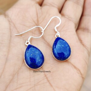May include: A pair of silver teardrop earrings with blue lapis lazuli stones. The earrings have a simple design and are perfect for everyday wear.