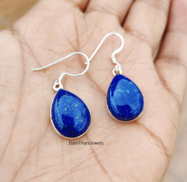May include: A pair of silver teardrop earrings with blue lapis lazuli stones. The earrings have a simple design and are perfect for everyday wear.