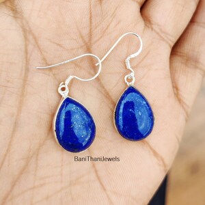 May include: A pair of silver teardrop earrings with blue lapis lazuli stones. The earrings have a simple design and are perfect for everyday wear.
