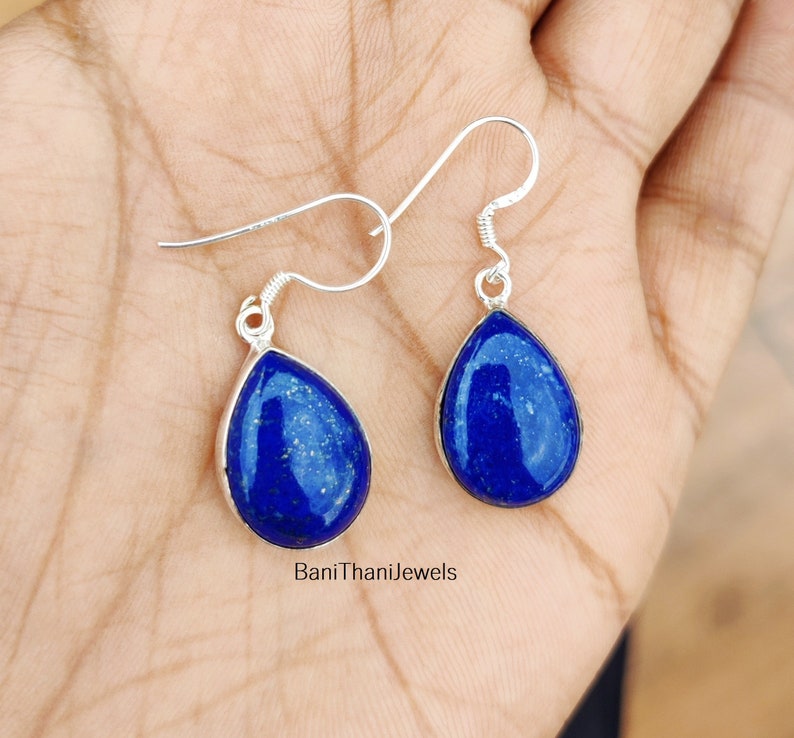 May include: A pair of silver teardrop earrings with blue lapis lazuli stones. The earrings have a simple design and are perfect for everyday wear.