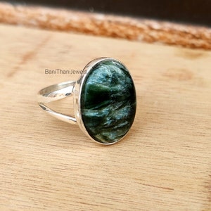 May include: A silver ring with a green and blue oval gemstone. The ring has a split band design. "BaniThaniJewels" is printed on the band.
