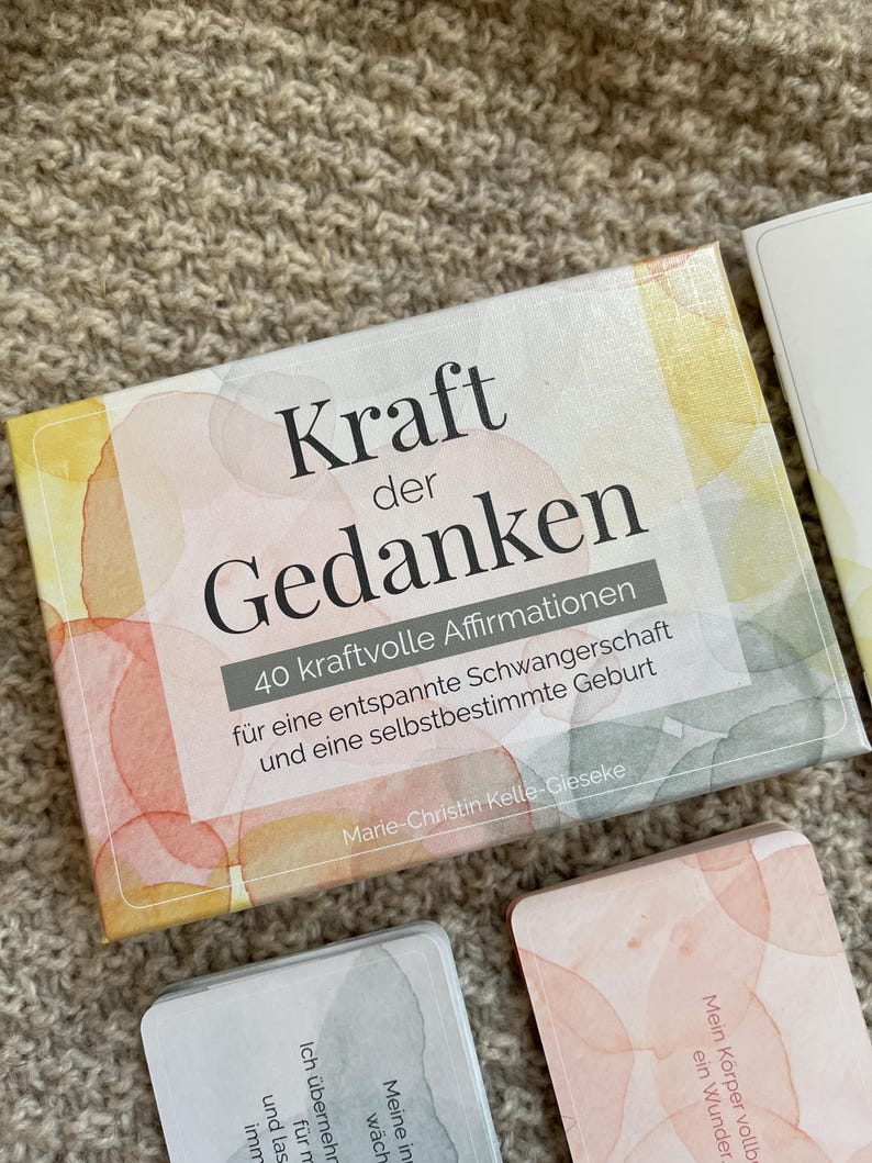 May include: A deck of affirmation cards titled "Kraft der Gedanken" (Power of Thoughts) with watercolor-style artwork. The box includes text in German, promoting a relaxed pregnancy and self-determined birth. Additional cards are visible.