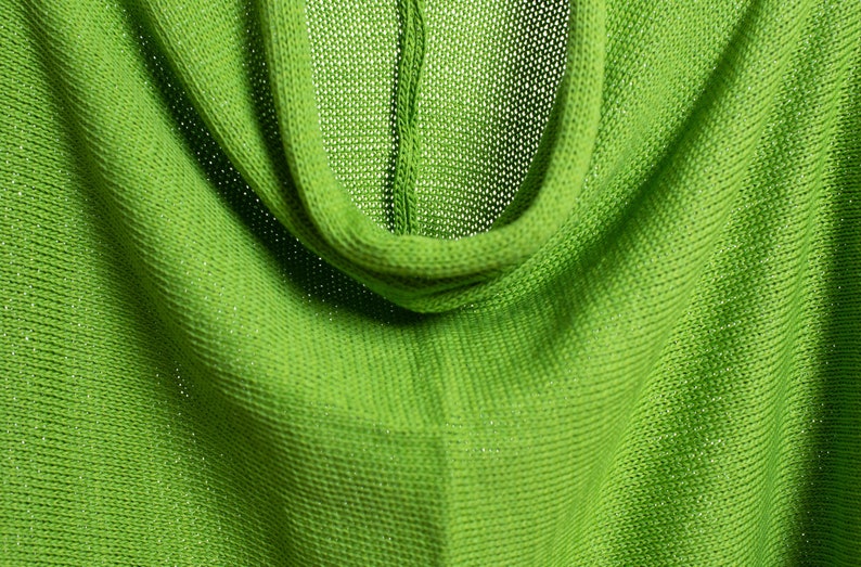 May include: Close-up of a green knitted fabric with a cowl neck. The fabric is soft and has a subtle sheen.