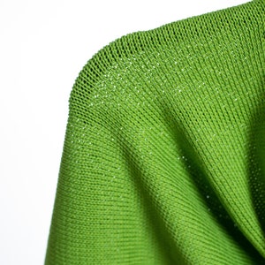 May include: Close-up of a bright green knitted fabric with a fine, even weave. The fabric is soft and pliable, with a slightly textured surface.