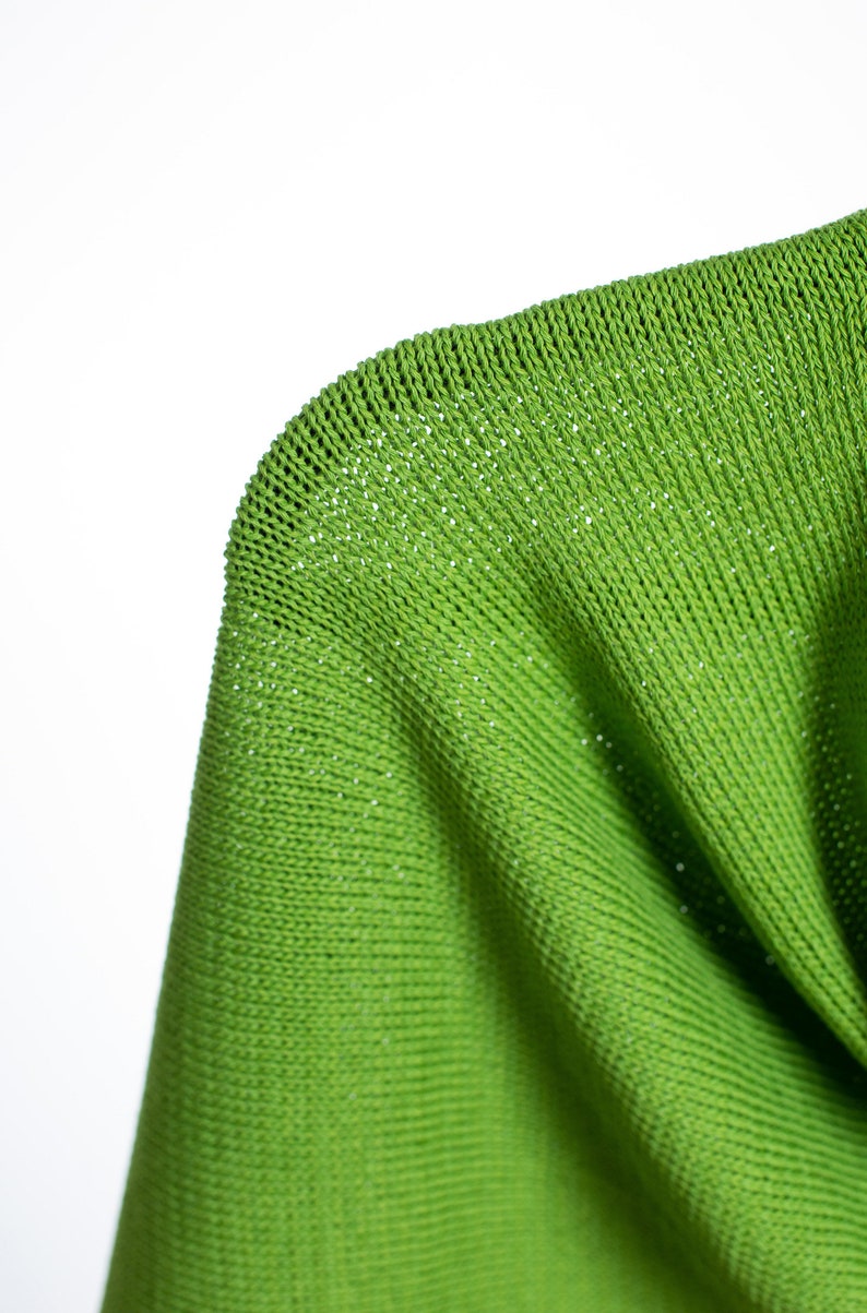May include: Close-up of a bright green knitted fabric with a fine, even weave. The fabric is soft and pliable, with a slightly textured surface.
