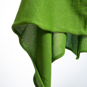 May include: A green knitted fabric draped over a white background. The fabric is textured and has a loose weave.