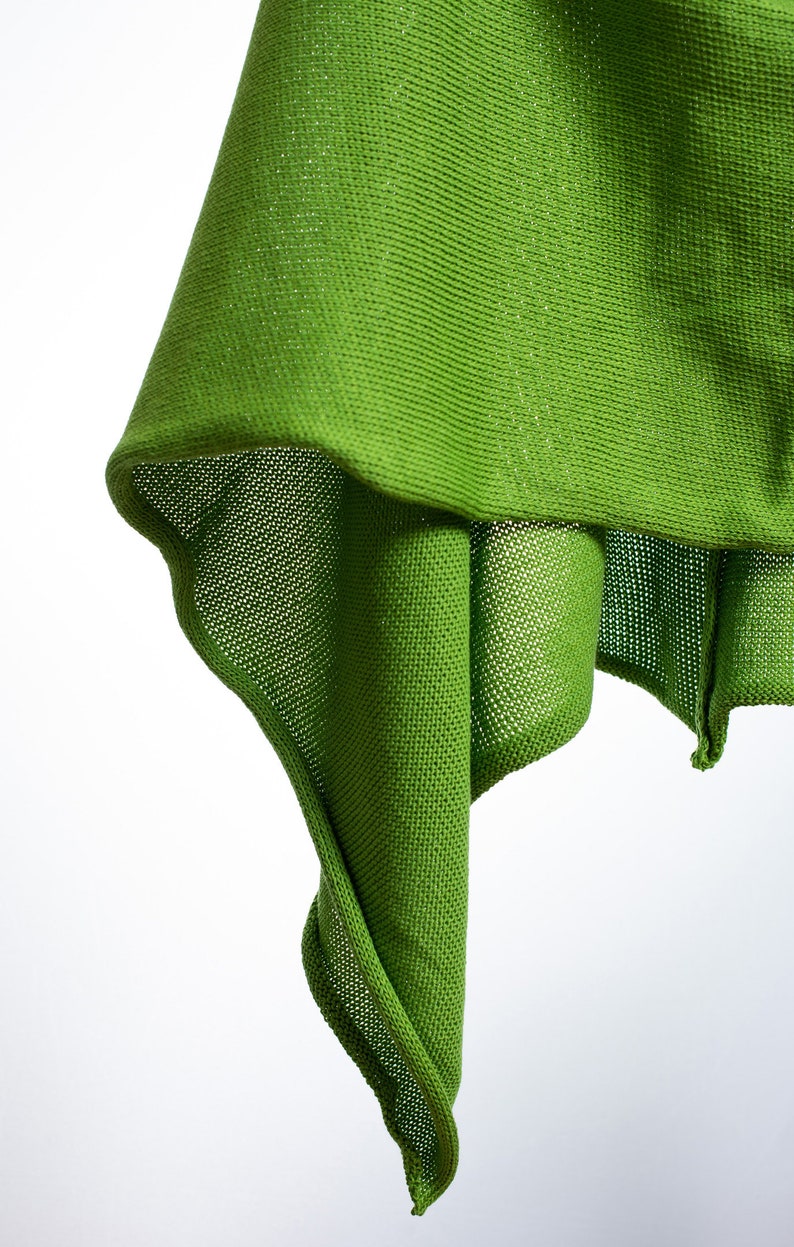 May include: A green knitted fabric draped over a white background. The fabric is textured and has a loose weave.