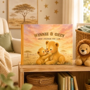 May include: A hardcover children's book titled Winnie & Ozzy Best Friends for Life, featuring an illustration of two lion cubs in a savanna at sunset. The cover displays warm orange and yellow hues, with the title text centered above the cubs.
