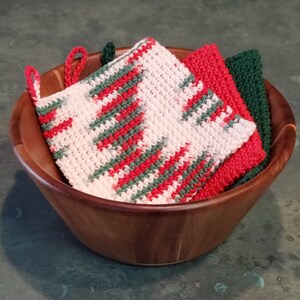 May include: A wooden bowl filled with three crocheted dishcloths. The dishcloths are pink, red, and green.