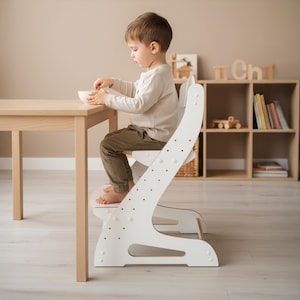 Peut inclure: Une chaise haute réglable en bois blanc avec un dossier incurvé et plusieurs réglages de hauteur pour le siège et le repose-pieds. La chaise présente un design de cadre incliné robuste et est placée à une table en bois clair.